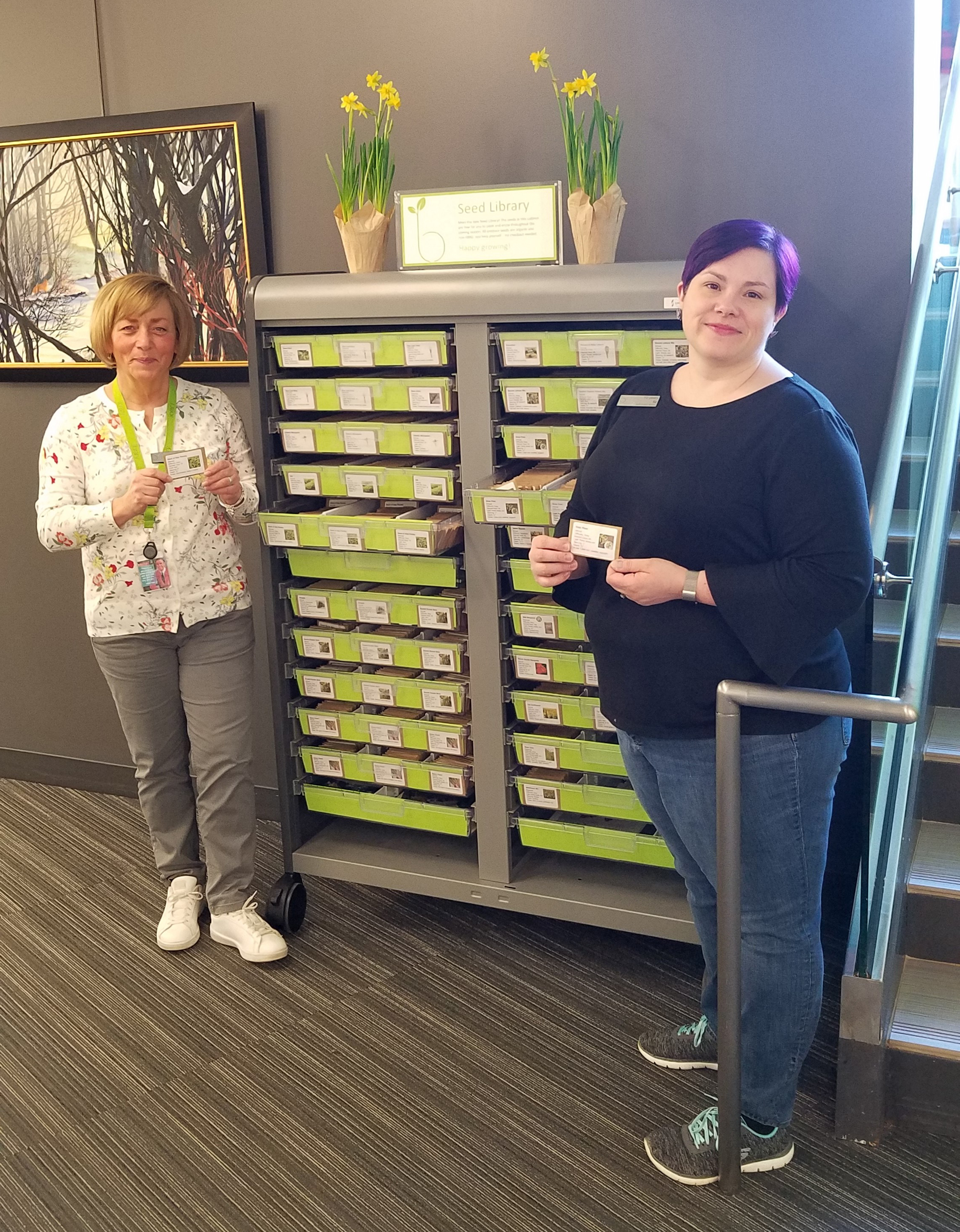 Seed Library cabinet with people on either side, holding packets of seeds