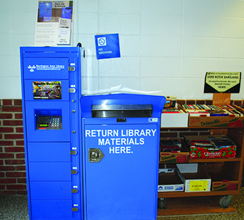 Photograph of bright blue automated lockers and book return in the train station building, display of used books for sale