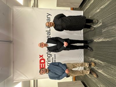 Three people stand, smiling, in front of a white banner that says TEDx BarringtonAreaLibrary