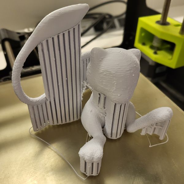 Mew printed in white filament on the Lulzbot 3D printer. Supports that will be removed later can be seen holding up overhangs like the tail, chin and feet.