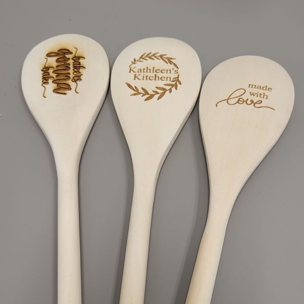 Three solid wood spoons etched with three different phrases: bakers gonna bake, Kathleen's Kitchen with a wreath around it, and made with love.