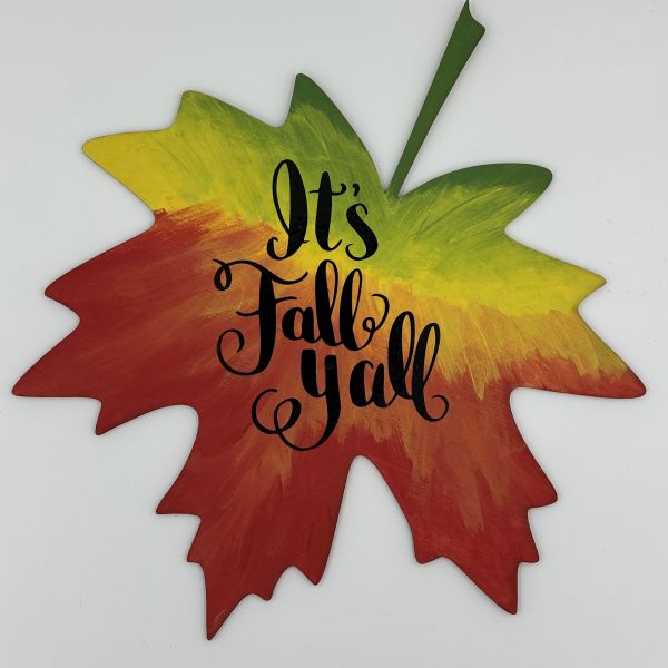Intricate phrase that says It's Fall Yall cut out of black vinyl and placed on a painted wood maple leaf with a red-yellow-green gradient.