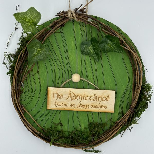 Green painted door with a doorknob in the middle. A sign that reads No admittance except on party business hangs from the doorknob. All around the door is moss, faux ivy, and grape vine twigs to make an earthy wreath.