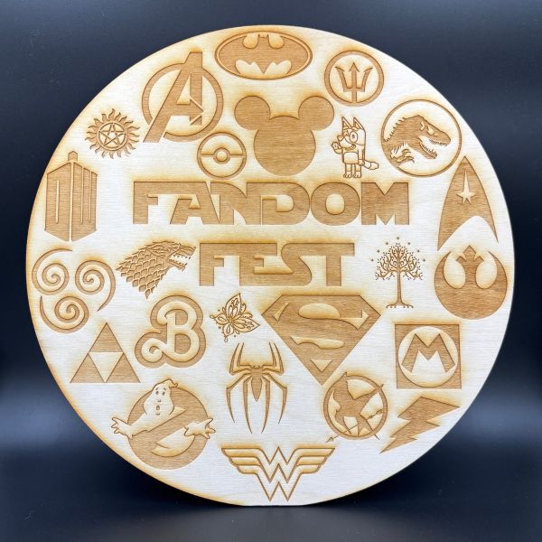 Round birch wood sign etched and cut on the laser. Various fandom logos are etched around the words Fandom Fest.