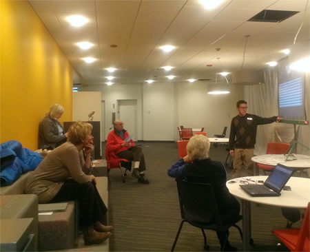 Male librarian stands at a projection screen, explaining something to four adult students