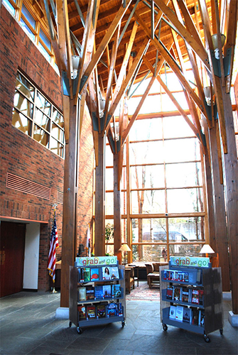 Photograph of Library atrium as it was in the early 2000s, book cart displays in center, seating and other furniture near the windows, soaring beams and tall windows